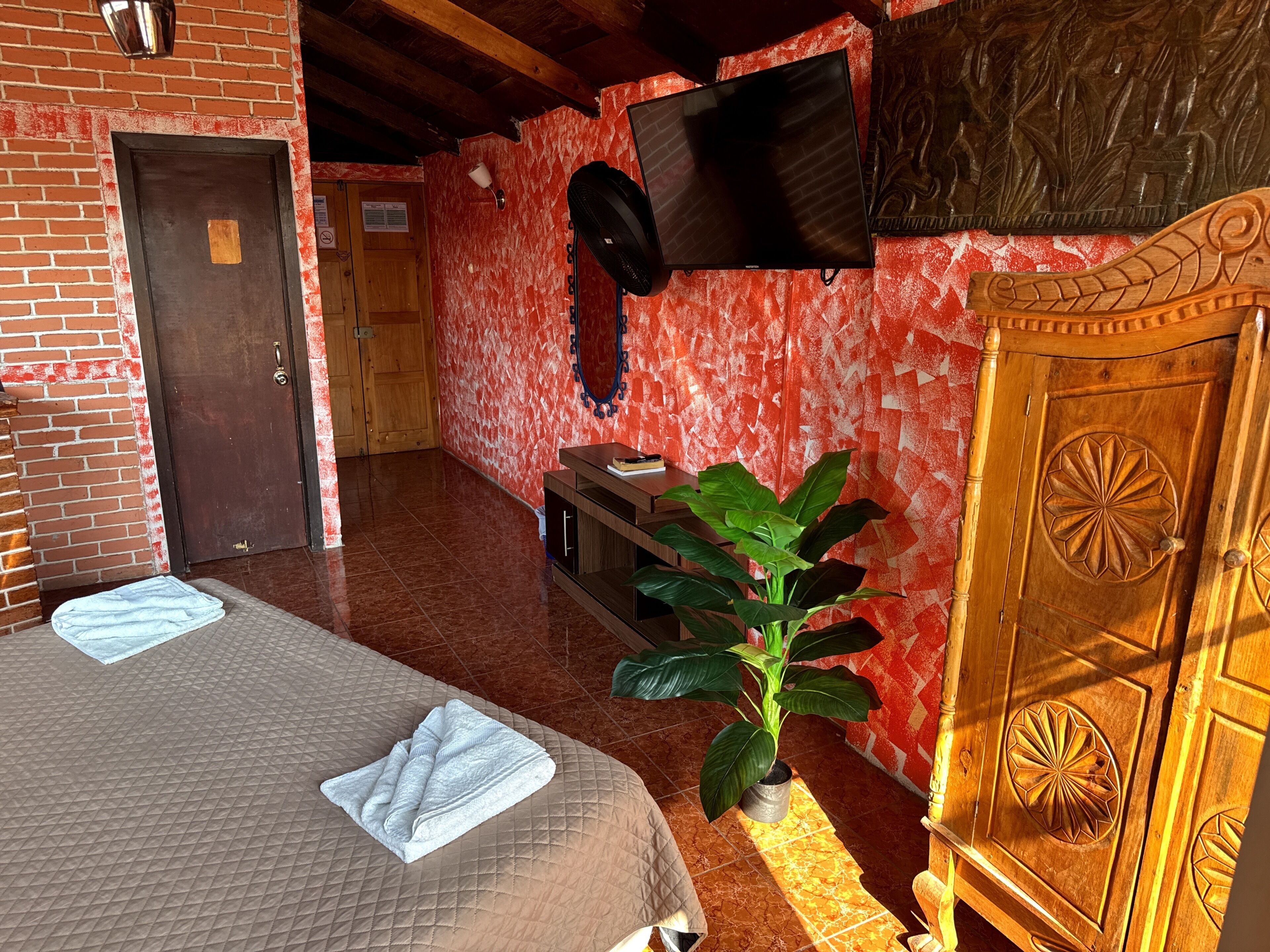 A hotel room with two beds, a TV, a wooden cabinet, and a potted plant.