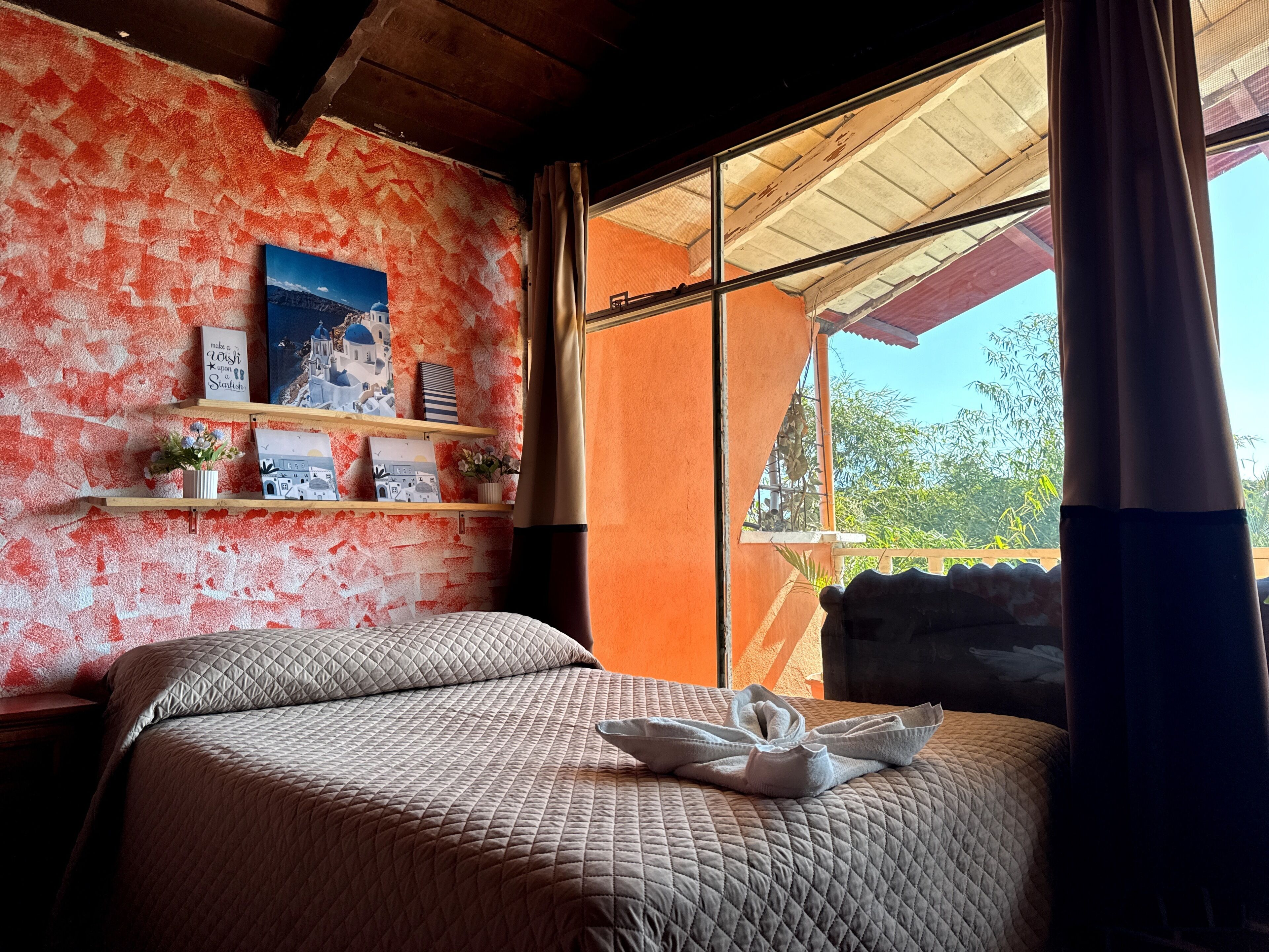A room with a bed, a window with curtains, a wall with a red and white pattern, and shelves with decorative items.