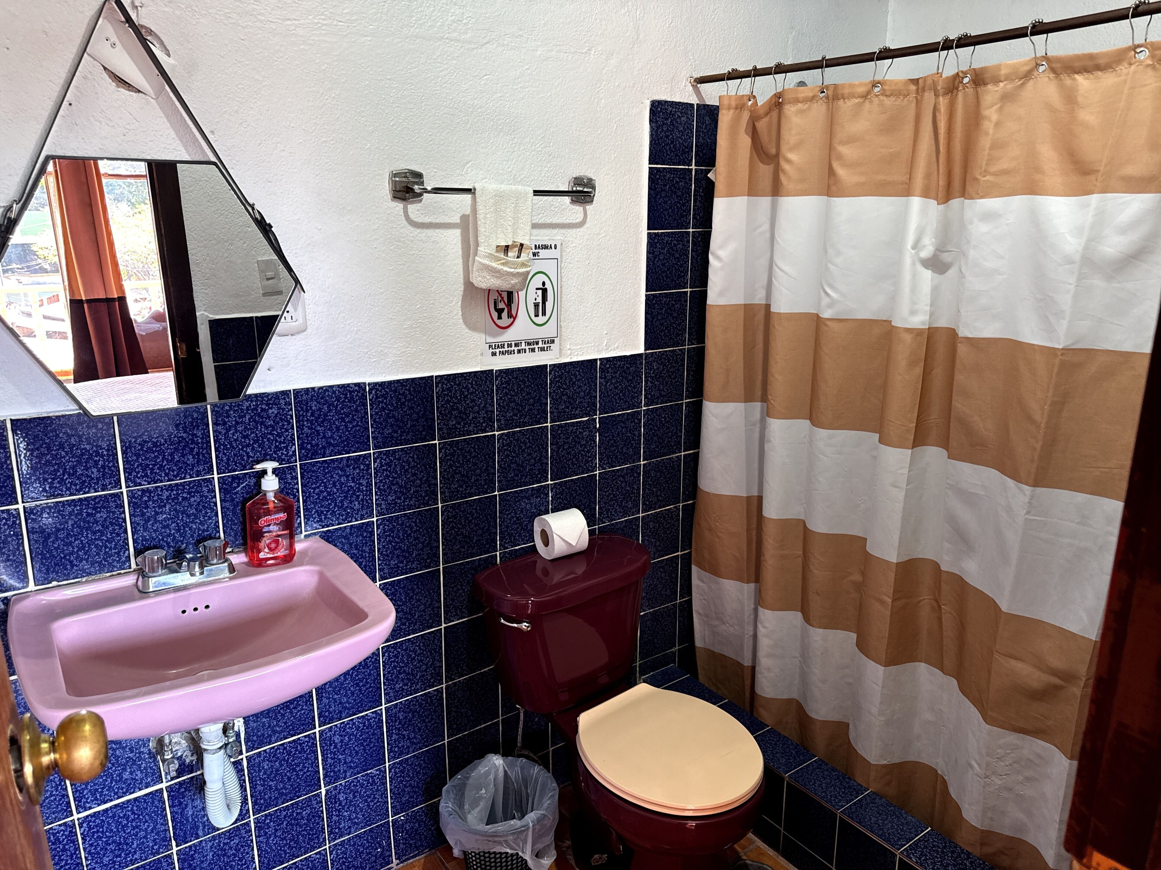 A bathroom with a pink sink, a toilet, a mirror, and a striped shower curtain.