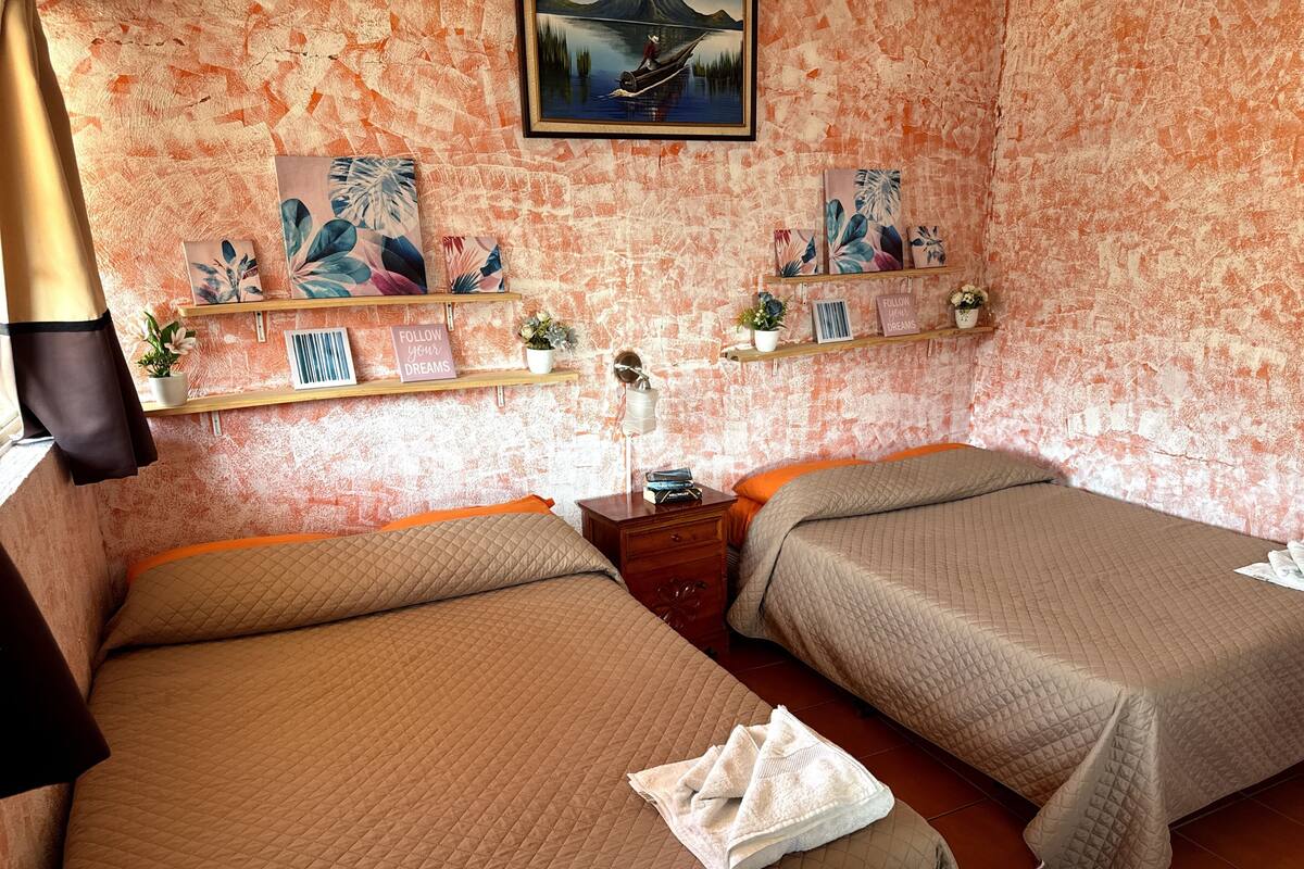 Een kamer met twee bedden, een schilderij, een plank met decoratieve objecten, en een bord waarop staat 'FOLLOW YOUR DREAMS'.