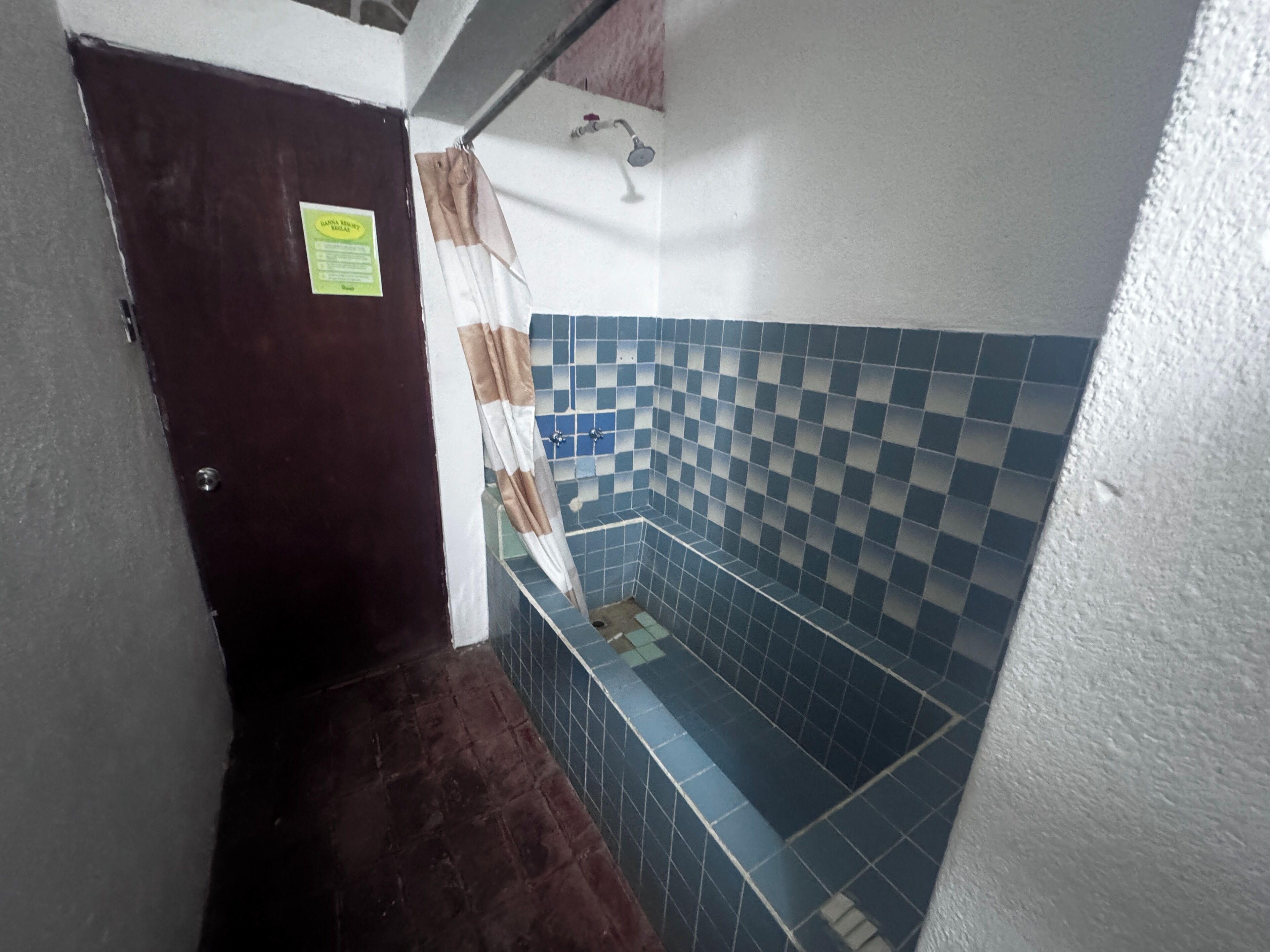 Une salle de bain avec des carreaux bleus à motifs, une douche et une porte sur laquelle est apposée une pancarte.