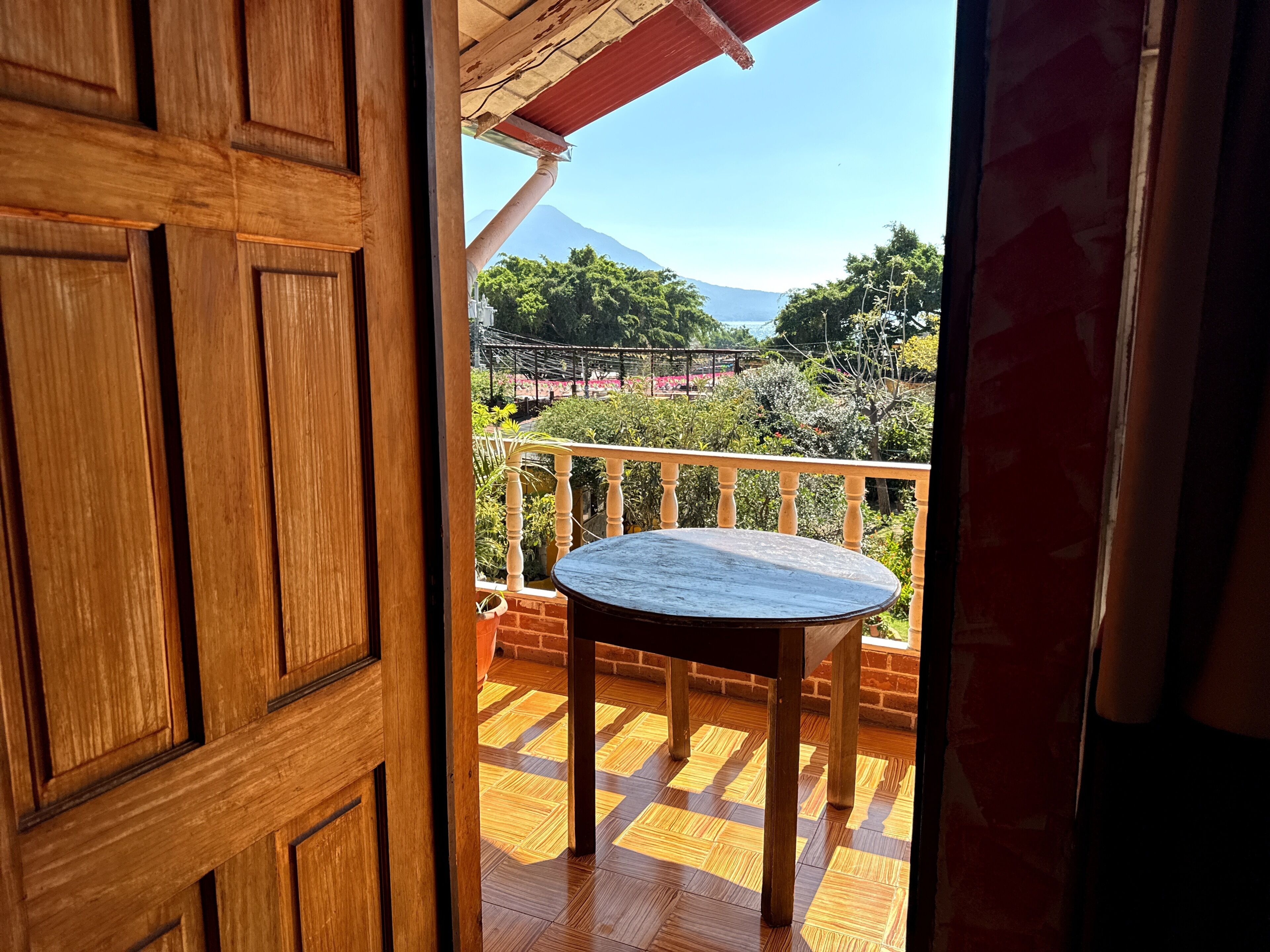 Une porte en bois donnant sur un balcon équipé d’une table et offrant une vue sur une montagne.