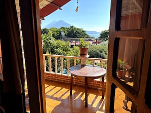 Un balcón con mesa de madera y plantas en macetas, con vistas a una montaña y vegetación.