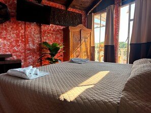 Una cama con cubrecolcha acolchado, un armario de madera, una planta en maceta y una ventana con cortinas.