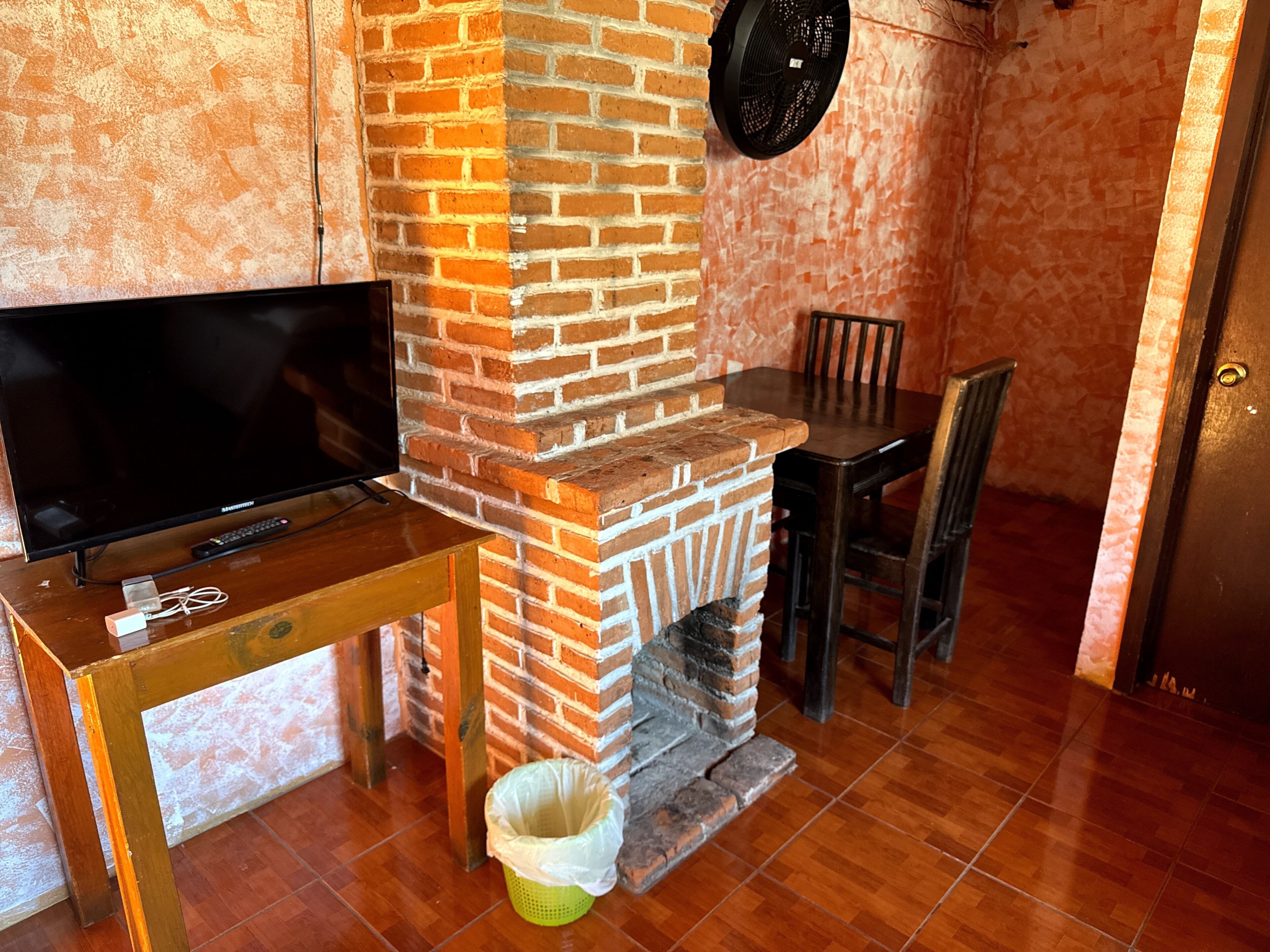 Una chimenea de ladrillo, un televisor sobre una mesa de madera, una silla y un cubo de basura.