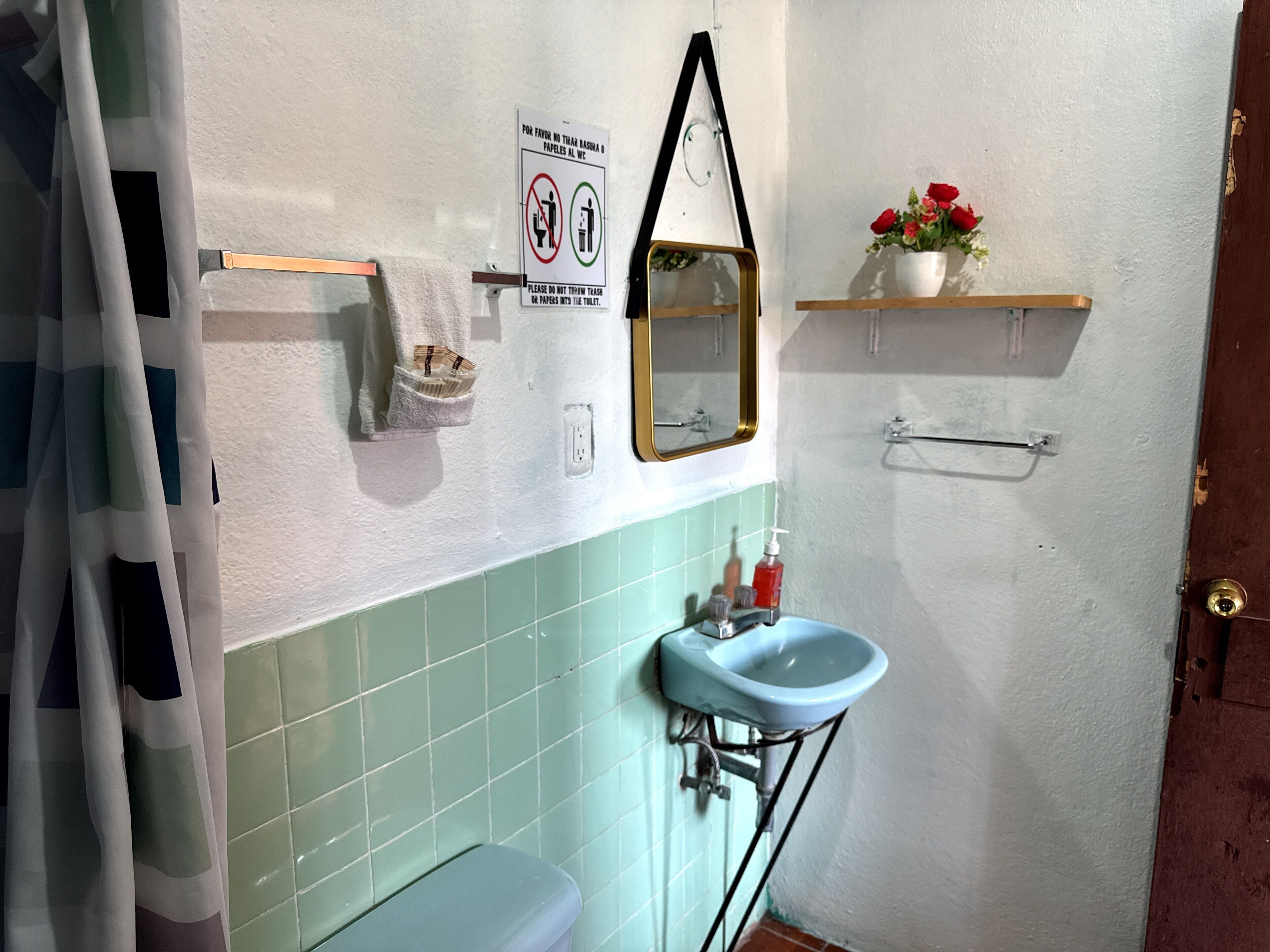 A bathroom with a toilet, sink, mirror, and a sign prohibiting flushing of trash or paper in the toilet.