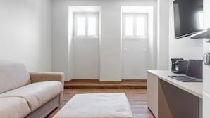 Una habitación moderna y minimalista con sofá, una mesita, televisor montado en la pared y una puerta con ventanas.