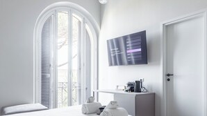 Un dormitorio moderno con una cama grande, un televisor montado en la pared y un balcón con contraventanas blancas.