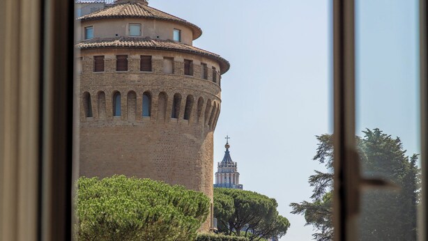 Vista a través de una ventana de un edificio histórico con una torre redonda y un campanario.