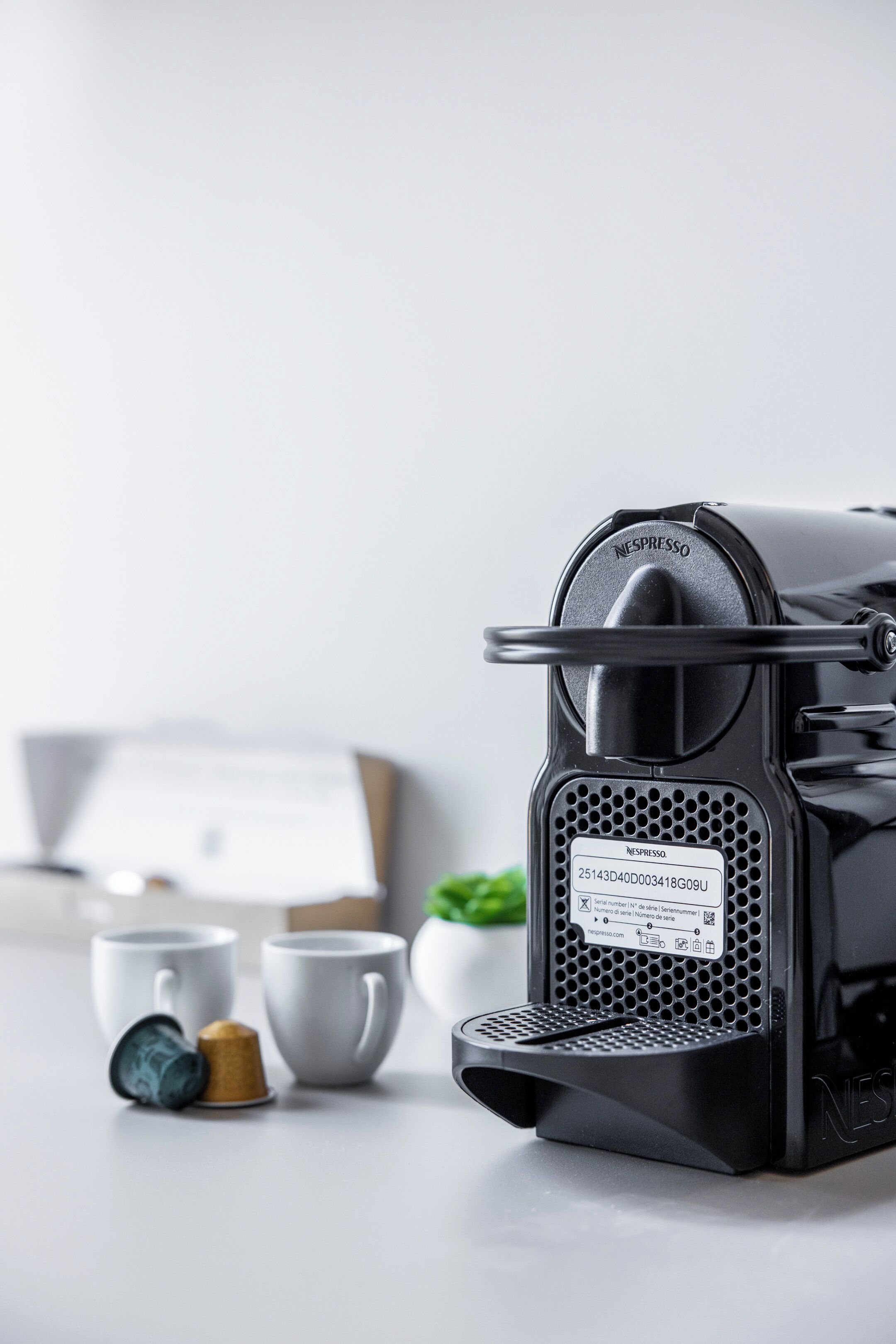 A Nespresso coffee machine with a coffee pod and two cups on a table.