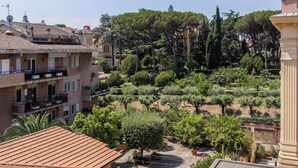 Un patio con techo de tejas, rodeado de edificios con balcones y un jardín con diversos árboles y arbustos.