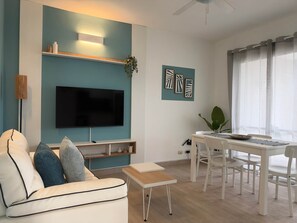 A modern living room with a flat-screen TV, a sofa, a coffee table, and a dining area with chairs and a table.
