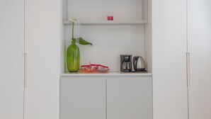 A kitchenette with a green vase, a coffee maker, and a red container on the countertop.