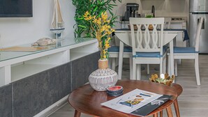 Uma cozinha moderna com armários brancos, uma área de refeições com mesa e cadeiras de madeira, e uma grande planta em vaso.