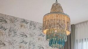 Quarto de hotel com cama, mesa de cabeceira, abajur, lustre decorativo e papel de parede floral.