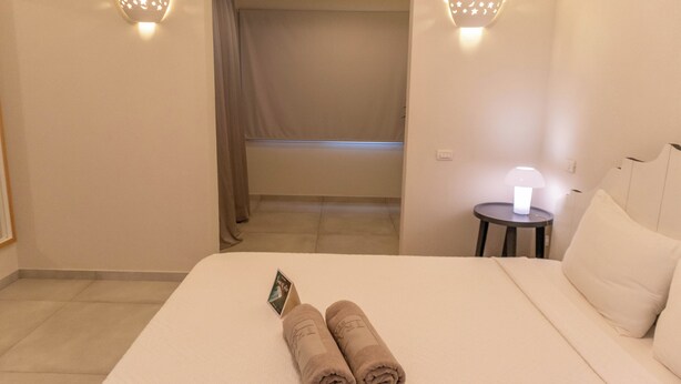 Une chambre d’hôtel avec un lit, deux serviettes enroulées, une table de chevet avec une lampe et une vue sur un balcon.