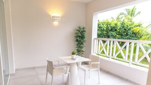Un balcon blanc avec une balustrade blanche, une table blanche avec deux chaises, un pot de fleurs et une vue sur la verdure à l’extérieur.