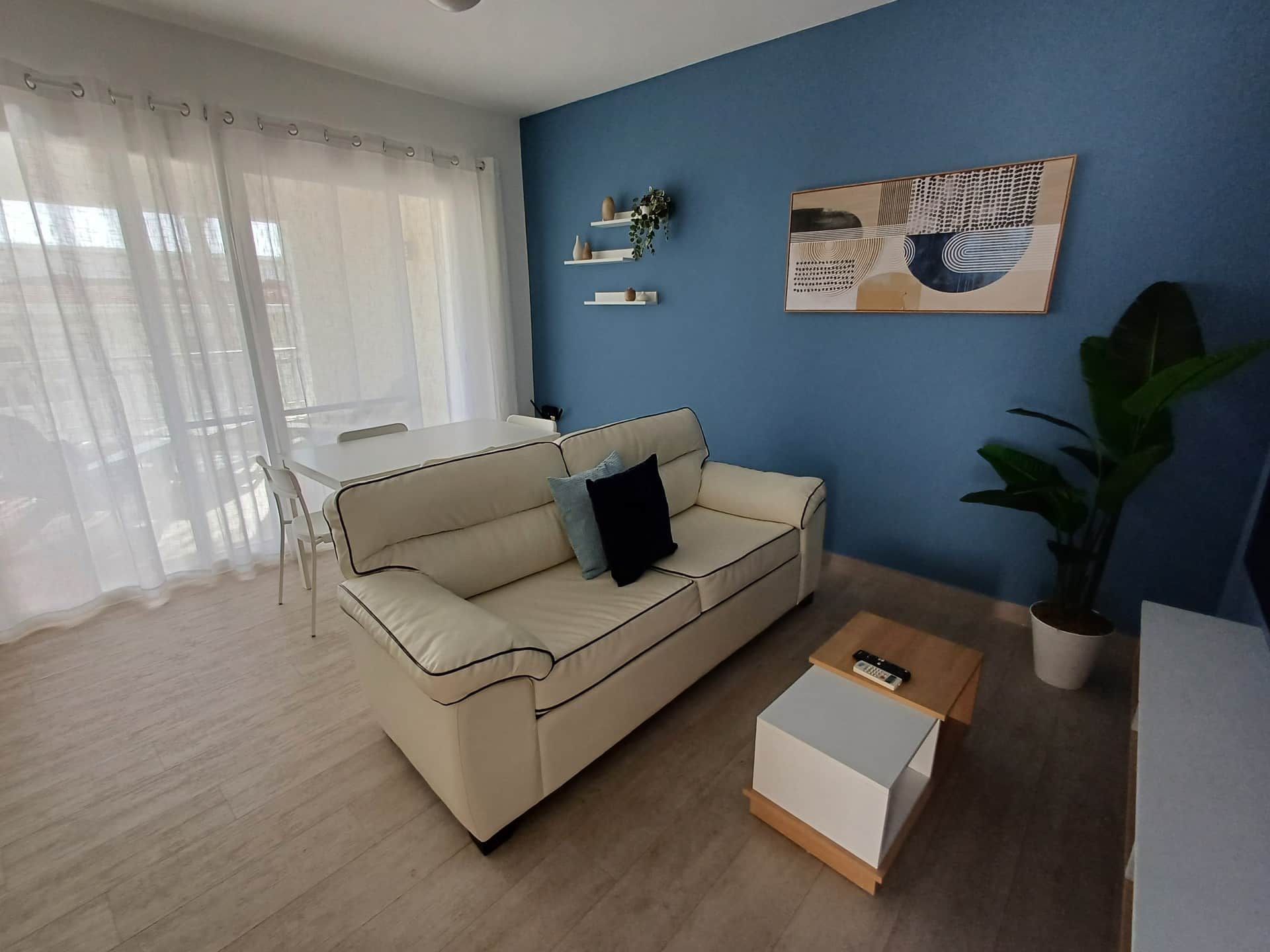 A living room with a beige sofa, a coffee table, a blue wall, and a painting.
