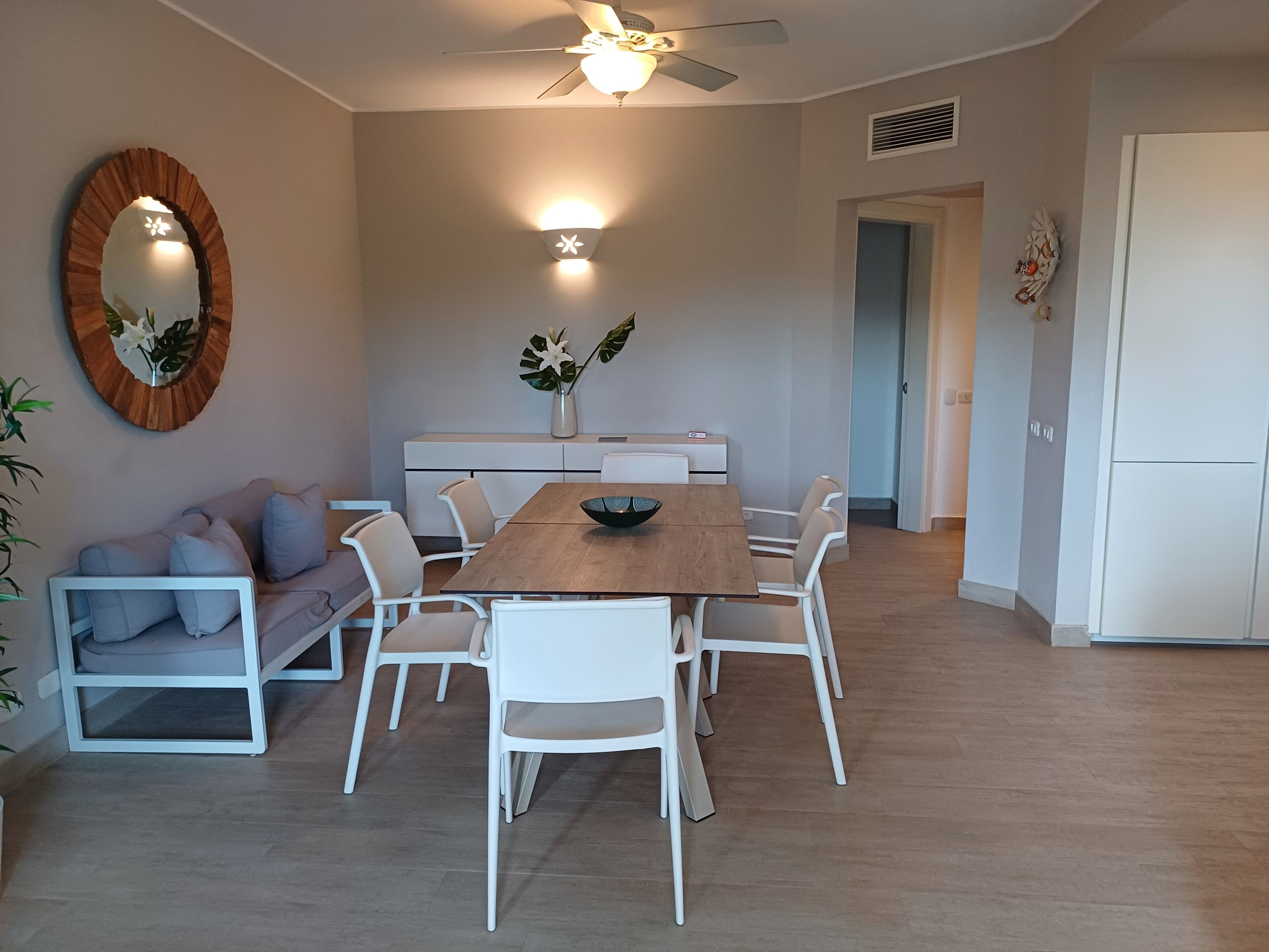 A modern dining area with a wooden table, white chairs, a sofa, and a ceiling fan.