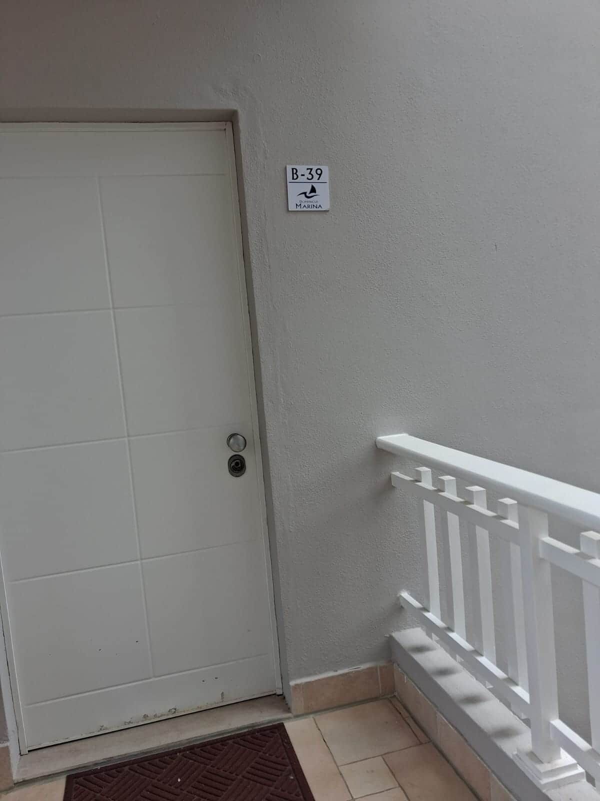 Une porte blanche avec une poignée en métal, une boîte aux lettres blanche et une rambarde blanche.