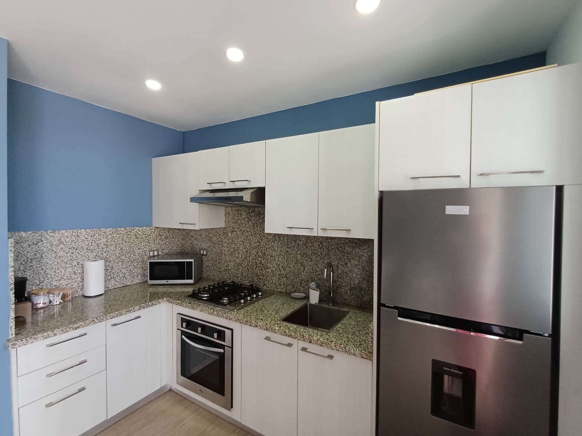 A compact kitchen with white cabinets, a stainless steel refrigerator, a microwave, and a gas stove.