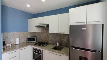 A compact kitchen with white cabinets, a stainless steel refrigerator, a microwave, and a gas stove.