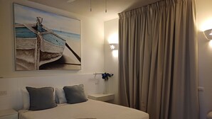 Siististi pedattu sänky, jonka päällä on pyyhe, jossa lukee ”TRACADERO BEACH RESORT”, ja seinällä on taulu, jossa on kuvattuna vene.