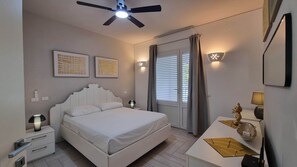 Une chambre à coucher comprenant un lit, des tables de chevet, un ventilateur de plafond, une fenêtre avec des rideaux et des lampes fixées au mur.