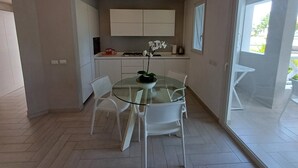 A modern kitchen with white cabinets, a glass dining table, and white chairs. - Tracadero Marina 49 Apt, 1 Hab. (Dominicus)