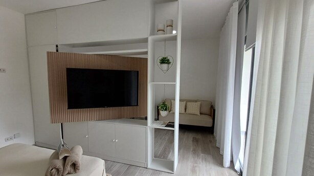 A modern bedroom with a bed, a TV mounted on a wall, a sofa, and a small table with a plant.