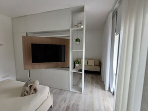 Een moderne slaapkamer met een bed, een aan de muur bevestigde televisie, een sofa en een bijzettafeltje met een plant.