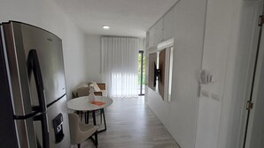 A modern kitchen with a built-in refrigerator, a dining area with a round table and chairs, and a sliding door leading to a balcony.