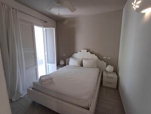A bedroom with a bed, a nightstand, a wall-mounted light fixture, and a window with curtains.