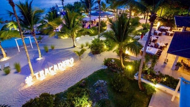 Un resort con vista a la playa, palmeras y zonas de estar al aire libre.