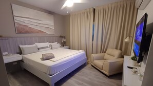 Una habitación de hotel moderna con una cama grande, una silla, un televisor y un ventilador de techo.