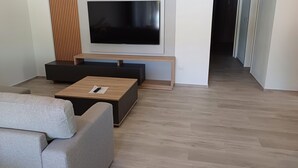 A modern living room with a flat-screen TV, a wooden coffee table, and a grey sofa.
