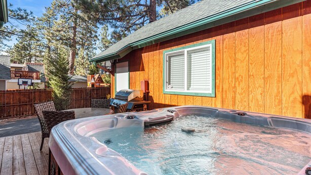 Un bain à remous sur une terrasse en bois, avec une maison en bois en arrière-plan.