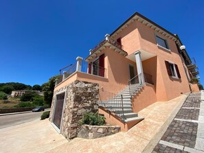 A two-story building with a stone foundation, a staircase leading to the upper floor, and a balcony with a railing. - Vacation home 10 km from the sea (Aglientu)
