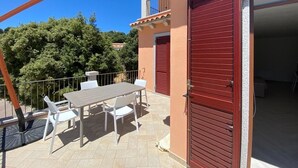 Une terrasse avec une table et des chaises, une porte de garage rouge et un balcon avec une balustrade.