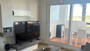Uma sala de estar moderna com uma TV de tela plana, um sofá, uma mesa de centro e uma varanda com área de estar externa.