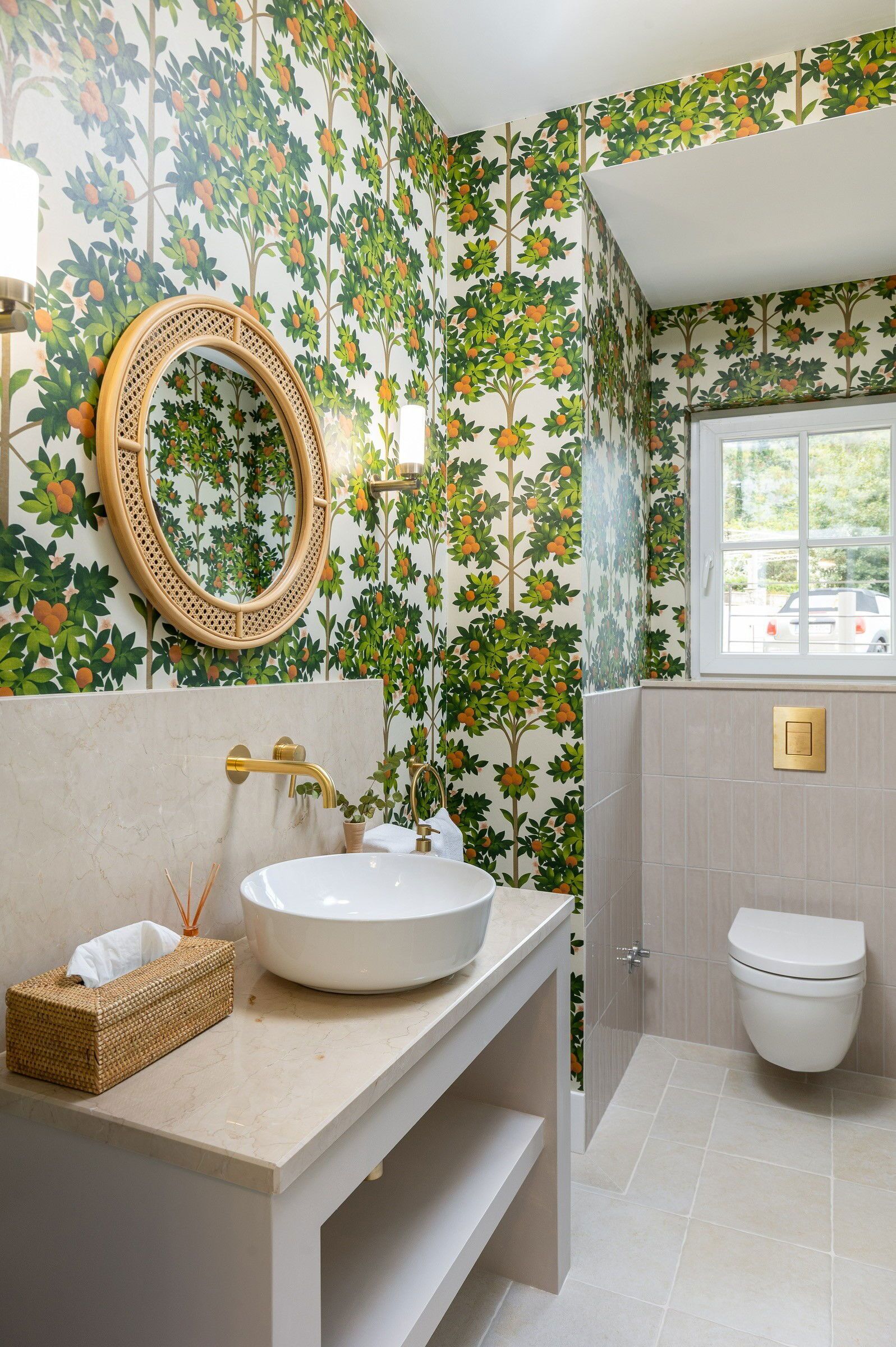 A bathroom with a floral wallpaper, a round mirror, a white sink, and a toilet.