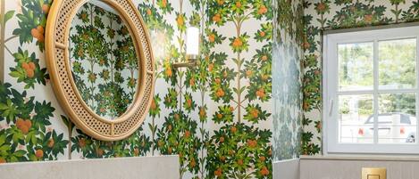 A bathroom with a floral wallpaper, a round mirror, a white sink, and a toilet.