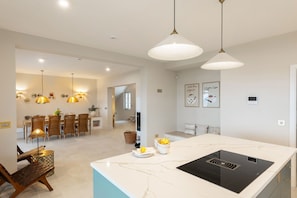 Una cocina moderna con una isla grande, iluminación colgante y un comedor con mobiliario de mimbre.