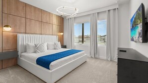 A modern bedroom with a large bed, wooden panel walls, a mounted TV, and a view of the outdoors. - HOGWARTS HEAVEN! Epic Private Theater! Mickey, Mario & Princess! (Orlando)