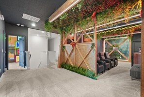 A reception area with a wooden reception desk, a seating area with chairs, and a wall decorated with plants and a mural. - Avatar Theater • Harry Potter Game Room • Toy Story & Marvel • Private Pool (Orlando)