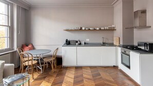 Une cuisine moderne avec des meubles blancs, un parquet en bois disposé en chevrons et un coin repas comprenant une table ronde et des chaises.