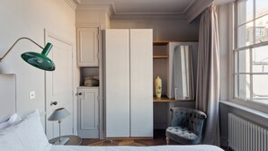 Une chambre à coucher comprenant un lit, une chaise, un bureau, une lampe, une armoire et une fenêtre.