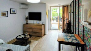 A living room with a sofa, a coffee table, a TV, a wooden cabinet, and a sliding glass door leading outside. - Magnificent Studio close to the sea. (Calvi)