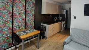 A compact living space with a dining table, a sofa, a kitchen area, and a colorful wall. - Magnificent Studio close to the sea. (Calvi)