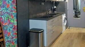 A modern kitchen with a built-in washing machine, a stainless steel trash bin, and a wooden floor. - Magnificent Studio close to the sea. (Calvi)